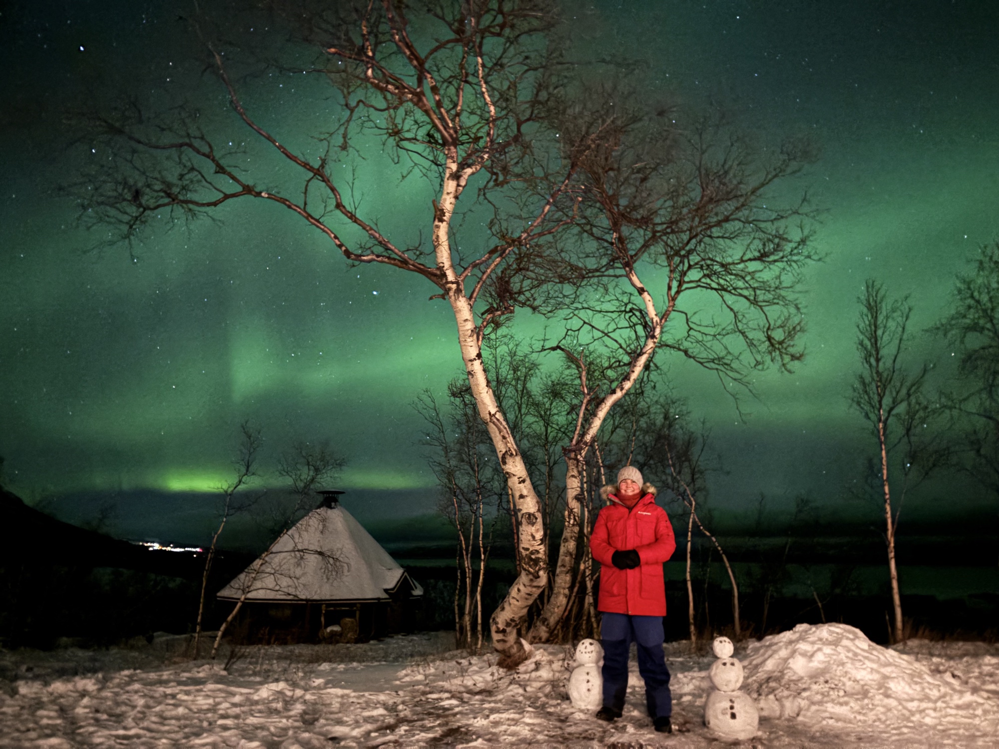 Jag framför ett träd och grönt norrsken i bakgrunden.